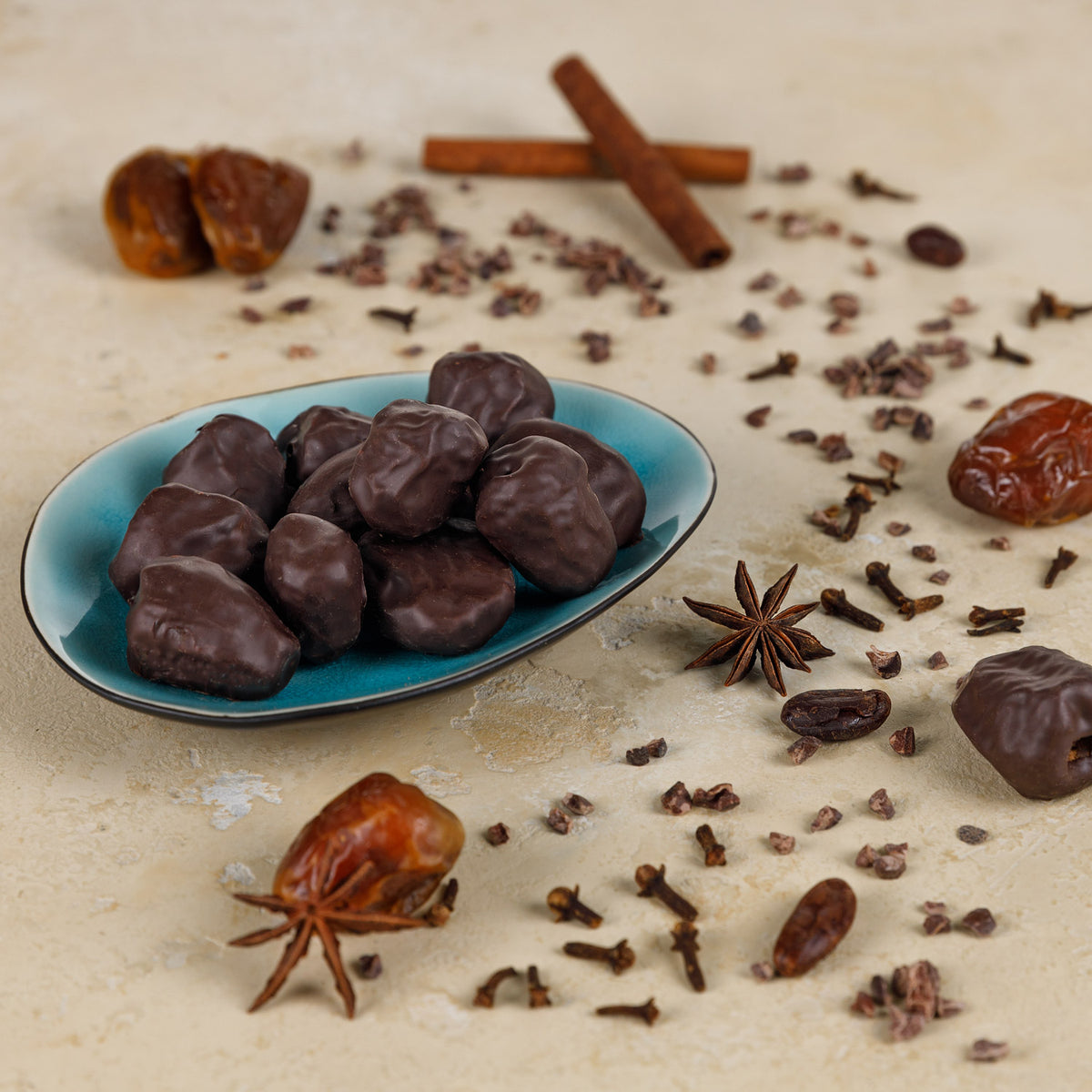 Leckere Datteln ummantelt von einer Schoko-Lebkuchenmischung knackig und unglaublich lecker. Schön angerichtet auf einem hellblauen Teller mit weihnachtlichem Gewürz im Hintergrund